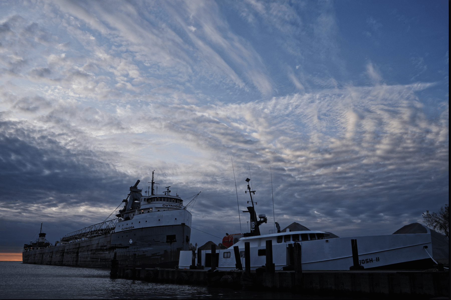 a Great self discharging freighter docked behind a fish tug at the Kingsville harbor with a partially cloudy blue sky in the background.