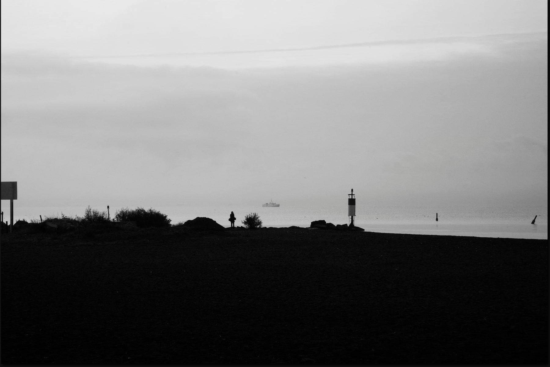 a silhouette of a photographer on a beach with a fish tug in the background
