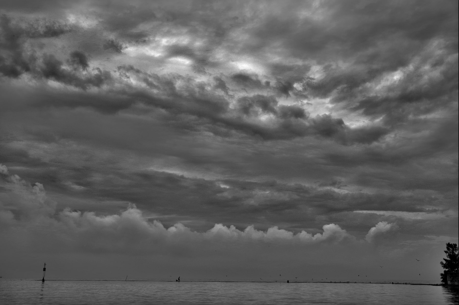a fisherman looking very small walking along a breakwater with a major storm approaching