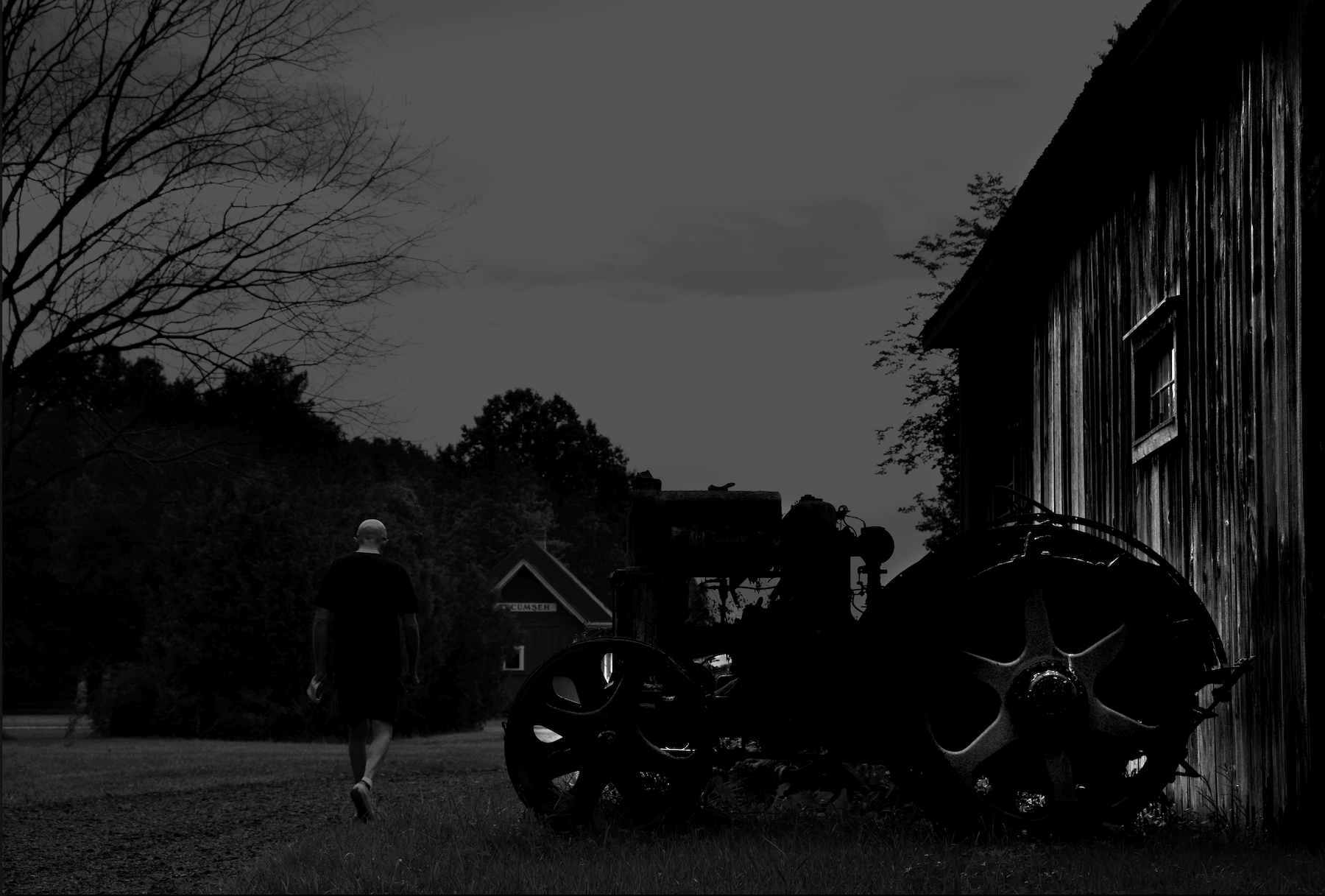 a silhouette of a man waking by an old farm tractor