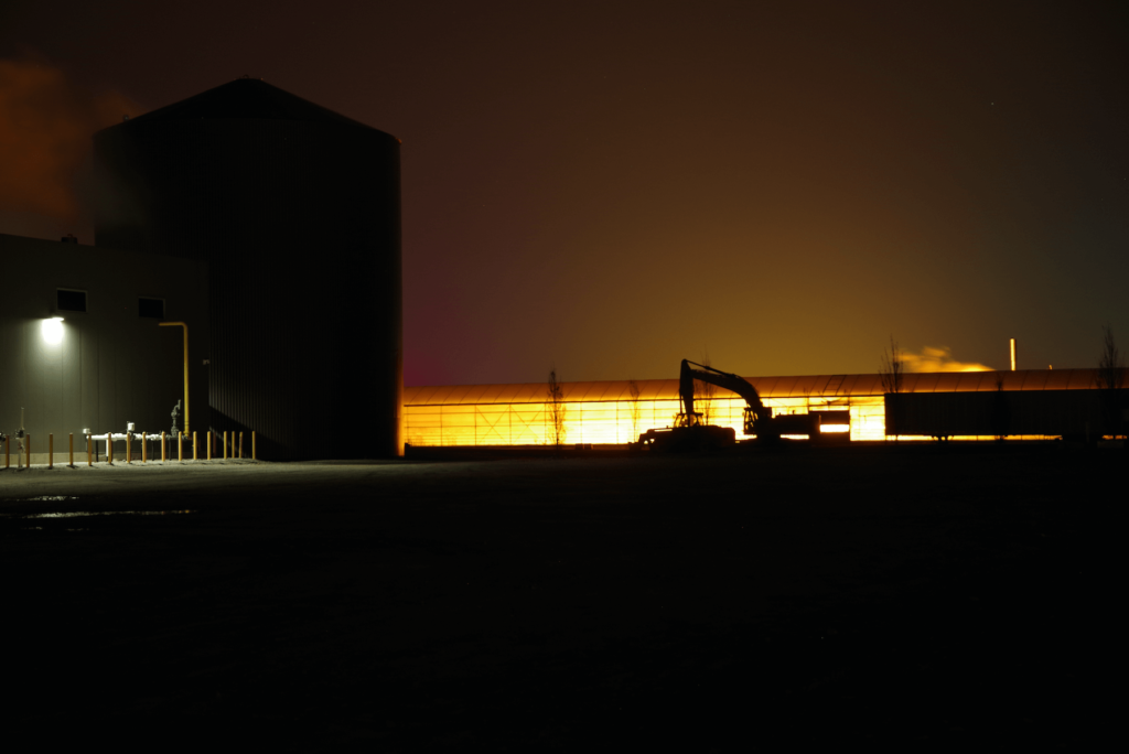 a silhouette track hoe backlit by a greenhouse