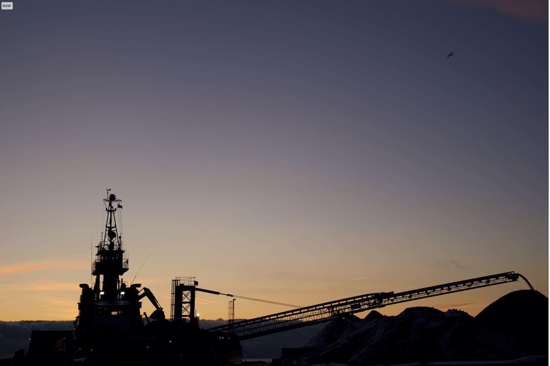 a silhouette of a conveyor belt attached to a great lakes freighter discharging aggregate at sunset