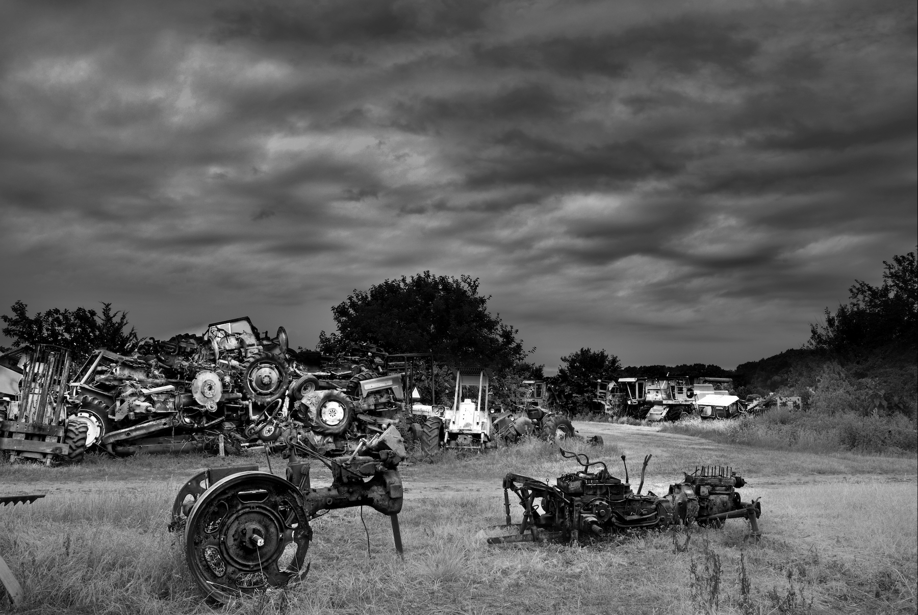 a big pile of broken tractors and engines with a angry sky in the background