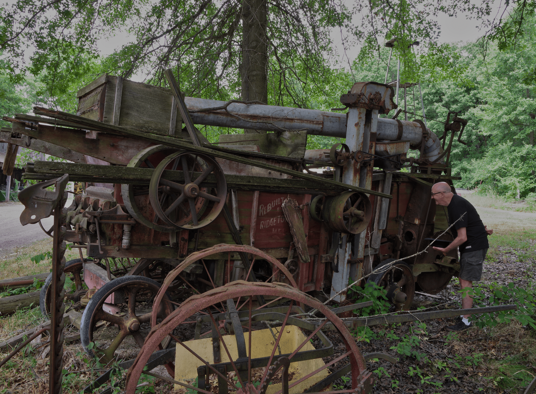 a picture of a bald man with a hat laughing at an old piece of farm equipment
