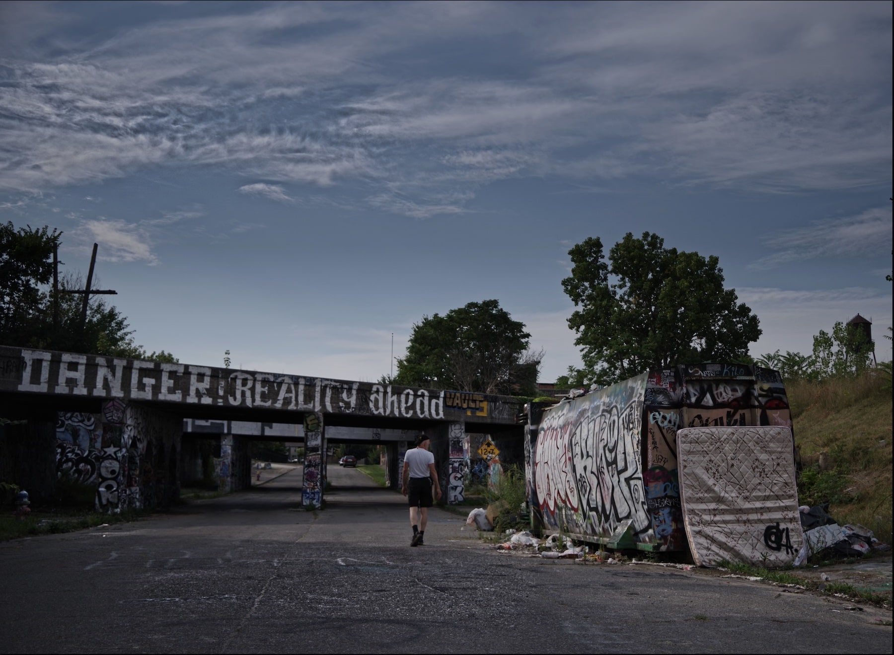 a man walking toward a graffiti covered train bridge in detroit